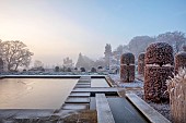BROUGHTON GRANGE GARDENS, OXFORDSHIRE: WINTER, FROST, JANUARY, RECTANGULAR POND, POOL, STEPPING STONES, RILL, CLIPPED BEECH TOPIARY