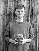 DAVID CARVER CROCUS COLLECTION DEVON: FEBRUARY, DAVID CARVER HOLDS TERRACOTTA CONTAINER WITH FLOWERS, BLOOMS OF CROCUS MIDAS TOUCH, BULBS, BLACK AND WHITE