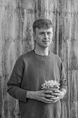 DAVID CARVER CROCUS COLLECTION DEVON: FEBRUARY, DAVID CARVER HOLDS TERRACOTTA CONTAINER WITH FLOWERS, BLOOMS OF CROCUS MIDAS TOUCH, BULBS, BLACK AND WHITE