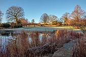 LITTLETHORPE MANOR, YORKSHIRE, FEBRUARY, WINTER GARDEN: LAKE, FROSTED PERENNIALS, GRASSES, LAWN, MANOR HOUSE