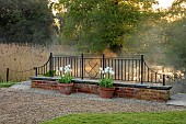 COUGHTON COURT, WARWICKSHIRE: MAY, MIST RISING OF POND, LAKE, MORNING LIGHT, TERRACOTTA CONTAINERS PLANTED WITH TULIP WORLD FRIENDSHIP, WALLED GARDEN