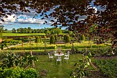 ASHBY MANOR HOUSE, NORTHAMPTONSHIRE: MAY, THE WALLED GARDEN, WILDFLOWERS, CLIPPED TOPIARY YEW, FOUNTAIN, WHITE TABLE, CHAIRS