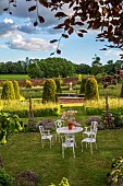 ASHBY MANOR HOUSE, NORTHAMPTONSHIRE: MAY, THE WALLED GARDEN, WILDFLOWERS, CLIPPED TOPIARY YEW, WHITE TABLE, CHAIRS