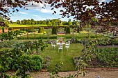 ASHBY MANOR HOUSE, NORTHAMPTONSHIRE: MAY, THE WALLED GARDEN, WILDFLOWERS, CLIPPED TOPIARY YEW, WHITE TABLE, CHAIRS
