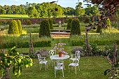 ASHBY MANOR HOUSE, NORTHAMPTONSHIRE: MAY, THE WALLED GARDEN, WILDFLOWERS, CLIPPED TOPIARY YEW, WHITE TABLE, CHAIRS