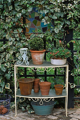 TERRACOTTA_POTS_ON_METAL__GLASS_ETAGERE_IN_FRONT_OF_IVY_CLAD_STAINED_GLASS_WINDOW_DESIGNER_JONATHAN_