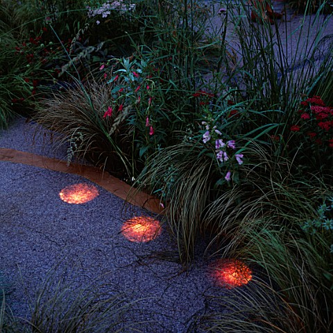 SPOTLIGHTS_BY_GARDEN__SECURITY_LIGHTING_SHINE_UPWARDS_THROUGH_GRAVEL_AT_THE_EDGE_OF_A_PATHWAY_IN_THE