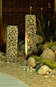 SIMPLE SCULPTURES OF TALL WIRE COLUMNS FILLED WITH STONES STAND AMONGST GRASSES AND GRAVEL IN MODERN ROOF GARDEN.  DESIGNER: STEPHEN WOODHAMS.