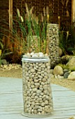 SIMPLE SCULPTURE OF TALL WIRE COLUMN FILLED WITH STONES STANDS ON WOODEN DECKING IN MODERN ROOF GARDEN.  DESIGNER: STEPHEN WOODHAMS.