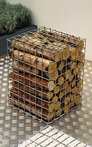 SCULPTURAL_FORM_OF_SIMPLE_WIRE_CUBE_FILLED_WITH_CUT_LOGS_STANDING_ON_METAL_DECKING_IN_MODERN_ROOF_GA