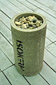 SIMPLE SCULPTURAL FORM OF CONCRETE CYLINDER FILLED WITH STONES STANDS ON WOODEN  DECKING IN MODERN ROOF GARDEN.  DESIGNER: STEPHEN WOODHAMS.