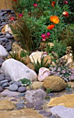 ORANGE POPPIES GROWING IN A DRY CREEK BED MADE WITH ROCKS AND PEBBLES. CERAMIC HEAD IS BY KEEYLA MEADOWS  CALIFORNIA