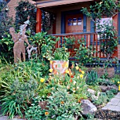PAINTED WOODEN HOUSE WITH VERANDAH OVERLOOKING THE FRONT GARDEN WITH SCULPTURE BESIDE WOMEN OF PARADISE POT AND TULIPS. DESIGN BY KEEYLA MEADOWS SAN FRANCISCO