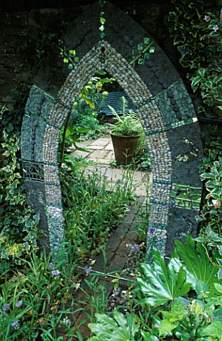 A_MOSAIC_MIRROR_WITH_SHELLS__PEBBLES_AND_TILES_IS_SURROUNDED_BY_HEDERA_GOLDHEART__POLEMONIUM_CAERULE