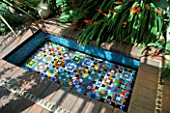 DECORATIVE FEATURE:  RECTANGULAR GLASS MOSAIC POOL SET INTO WOODEN DECKING TERRACE  FILLED WITH CLEAR WATER AND DESIGNED BY KARLA NEWELL