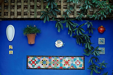 BRIGHTLY_COLOURED_MOSAIC_SET_IN_ULTRAMARINE_BLUE_WALL_BENEATH_ON_A_WOODEN_BENCH_ARE_ORANGE_AND_RED_C