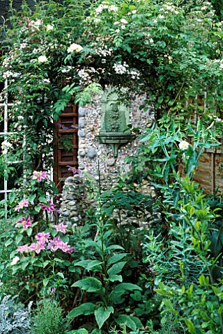 SMALL_TOWN_GARDEN_VIEW_THROUGH_SHADY_ARCH_TO_WALL_MOUNTED_FOUNTAIN_IN_FLINT__SHELL_GROTTO_JASMINUM_O