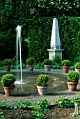 FOUNTAIN SURROUNDED BY BUXUS SEMPERVIRENS IN POTS WITH A STONE OBELISK BEHIND.  ARROW COTTAGE  HEREFORDSHIRE