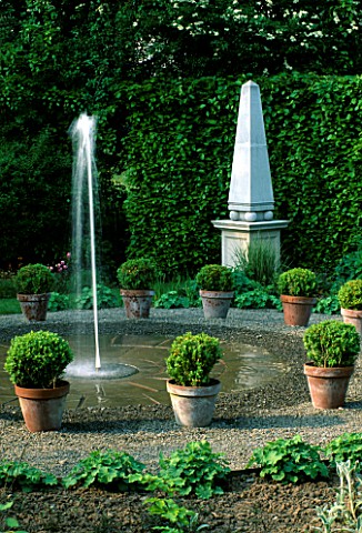 FOUNTAIN_SURROUNDED_BY_BUXUS_SEMPERVIRENS_IN_POTS_WITH_A_STONE_OBELISK_BEHIND__ARROW_COTTAGE__HEREFO
