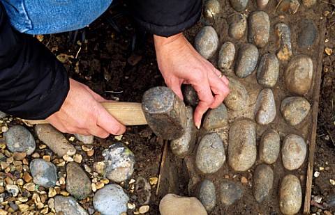 LOUISE_GENTLY_HAMMERS_A_PEBBLE_INTO_THE_CEMENT_BASE