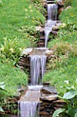 WATER FEATURE: WATER CASCADES THROUGH MEADOW WITH PRIMULA PULVERULENTA AND CAREX MORROWII  IN THE WYEVALE/ PORTMEIRION GARDEN  CHELSEA 99