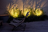 TIMBER DECKING AND DECK CHAIRS WITH THE FOUNTAIN GRASS - PENNISETUM ALOPECUROIDES - BEHIND LIT UP. DESIGNERS PAUL THOMPSON AND TREVYN MCDOWELL. SHADOW