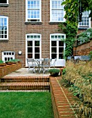 VIEW FROM LAWN TOWARDS HOUSE WITH METAL GARDEN FURNITURE ON RAISED PATIO. A BORDER OF STIPAS INPLANTED IN A RAISED BED. MODERNISTS TOWN GARDEN DESIGNED BY CHRISTOPHER BRADLEY-HOLE.