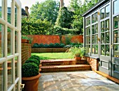 VIEW THROUGH PATIO DOOR PAST CONSERVATORY TOWARDS THE LAWN. WITH BOX BALLS IN RAISED BRICK BED AND ITALIAN POLISHED PLASTER WALL. MODERNISTS TOWN GARDEN DESIGNED BY C. BRADLEY-HOLE