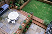 OVERVIEW OF GARDEN WITH METAL GARDEN FURNITURE  LAWN  PAVING SLABS AND BRICK WORK. TERRACOTTA CONTAINERS HOLD BOX BALLS. MODERNISTS TOWN GARDEN DESIGNED BY CHRISTOPHER BRADLEY-HOLE