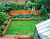 OVERVIEW OF GARDEN WITH CONSERVATORY  LAWN EDGED WITH RAISED BRICK BED OF BOX BALLS &  GRASSES AND TERRACOTTA COLOURED ITALIAN POLISHED PLASTER WALL. MODERNISTS TOWN GARDEN.