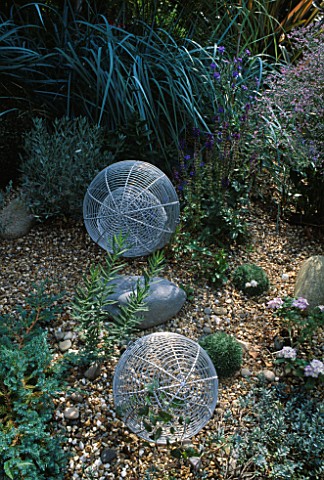 ALUMINIUM_GLOBES_STANDING_ON_GRAVEL_AND_SURROUNDED_BY_GREY_GRASSES__CONVULULUS_CNEORUM_AND_LOBELIA_S