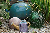 TURQUOISE CERAMIC BALLS  FISHING FLOATS AND A SPANISH CERAMIC WATERING CAN STAND ON GRAVEL. ROBIN GREEN AND RALPH CADES SEASIDE STYLE GARDEN  LONDON