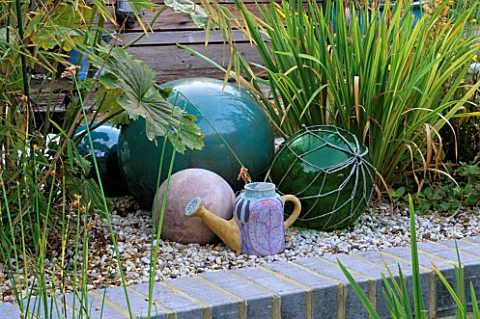 TURQUOISE_CERAMIC_BALLS__FISHING_FLOATS_AND_A_SPANISH_CERAMIC_WATERING_CAN_STAND_ON_GRAVEL_ROBIN_GRE