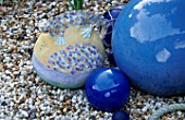 A CERAMIC SALAMANDER JUG INSPIRED BY GAUDI WITH COBALT CERAMIC AND GLASS BALLS ON A BED OF SHINGLE. ROBIN GREEN AND RALPH CADES SEASIDE STYLE GARDEN  LONDON