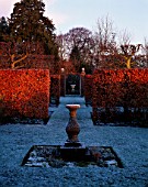 A STONE SUNDIAL CREATES A FOCAL POINT IN THE FROSTED GARDEN  WHILST WINTER SUNLIGHT HIGHLIGHTS THE COLOUR OF THE BEECH HEDGES. WOLLERTON OLD HALL  SHROPSHIRE.