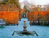 A STONE SUNDIAL CREATES A FOCAL POINT IN THE FROSTED GARDEN  WHILST WINTER SUNLIGHT HIGHLIGHTS THE COLOUR OF THE BEECH HEDGES. WOLLERTON OLD HALL  SHROPSHIRE.