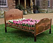 WOODEN BED FRAME WITH POTS OF HYACINTH CARNEGIE MAKING UP THE BED COVERS. DESIGNED BY IVAN HICKS. GROOMBRIDGE PLACE  KENT.