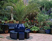 CRAZY PAVING PATIO PAINTED WITH A SOFT TERRACOTTA MASONRY PAINT WITH COBALT BLUE POTS AND SEAT AND FOLIAGE PLANTS. ROBIN GREEN AND RALPH CADES SEASIDE STYLE GARDEN  LONDON