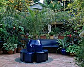 CRAZY PAVING PATIO PAINTED WITH SOFT TERRACOTTA MASONRY PAINT WITH COBALT BLUE POTS  SEAT AND FOLIAGE PLANTS. ROBIN GREEN AND RALPH CADES SEASIDE STYLE GARDEN  LONDON