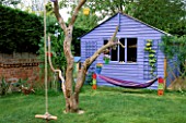 THE CHILDRENS PLAY AREA WITH BLUE SUMMERHOUSE  BLACKBOARD  HAMMOCK  TURF CROCODILE AND OLD TREE. DESIGN BY CLARE MATTHEWS