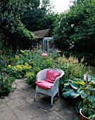 WICKER CHAIR WITH PINK CUSHION ON STONE TERRACE WITH SHED IN THE BACKGROUND. HAMPTON COTTAGE  SUSSEX