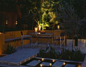 A PLACE TO SIT: ALUMINIUM TABLE AND CHAIRS ON PATIO SURROUNDED BY YELLOW RENDERED WALLS WITH RAISED BEDS AND RILL. .EVENING LIGHTING WITH CANDLES AND LANTERNS. DESIGNER JOE SWIFT