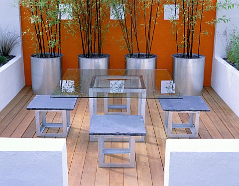MINIMALIST_GARDEN_BY_WYNNIATTHUSEY_CLARKE_GLASS_TABLE_WITH_METAL_AND_SLATE_CHAIRS_ON_WOODEN_DECKING_