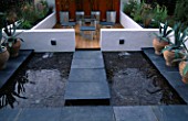 MINIMALIST GARDEN BY WYNNIATT-HUSEY CLARKE: CONCRETE WALLS  WATER  GLASS TABLE  ORANGE PAINTED CONCRETE WALL AND GALVANISED CONTAINERS WITH BLACK STEMMED BAMBOO-PHYLLOSTACHYS NIGRA