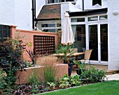 DECKED TERRACE WITH TABLE AND CHAIRS  RAISED BED WITH PHORMIUM  RENDERED WALLS PAINTED TERRACOTTA. DESIGNER: SARAH LAYTON