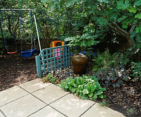 CHILDRENS_GARDEN_SWINGS_WITH_BARK_BENEATH__BLUE_TRELLIS_SCREEN__WATER_FEATURE_WITH_FATSIA_JAPONICA_B