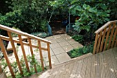 VIEW ONTO CHILDRENS GARDEN FROM DECKED TERRACE: SWINGS WITH BARK BENEATH  BLUE TRELLIS SCREENS  PAVING  WOODEN SEAT  FIG. DESIGNER: SARAH LAYTON