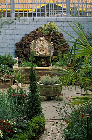 VIEW_ALONG_GARDEN_PAST_BOX_AND_TRACHYCARPUS_TO_WATER_FEATURE_MADE_OF_BRICK_WALL_AND__BRIGHTON_PIER_G