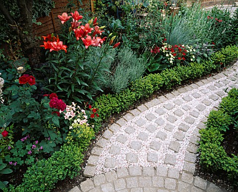 CURVING_PATH_WITH_BRICK_SETTS_AND_PINK_GRAVEL_MULCH_SURROUNDED_BY_BOX_BALLS__RED_LILIES___ROSES_AND_