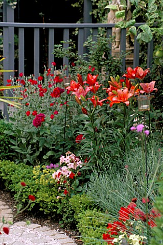 CURVING_PATH_WITH_BRICK_SETTS_AND_PINK_GRAVEL_MULCH_SURROUNDED_BY_BOX_BALLS__RED_LILIES___ROSES__NIC